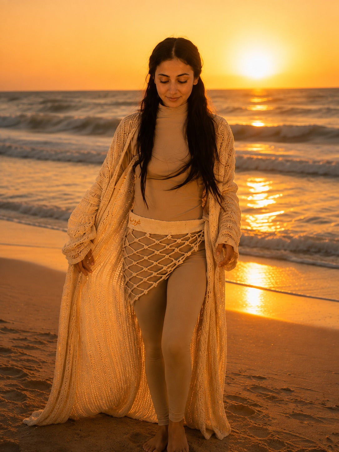 Model wearing the Ghoroub Cardigan in Sunset Ivory · Gold with the Waist Wrap, full-length front view on the beach at sunset.