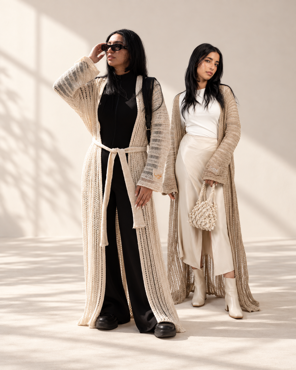 Two women wearing the Ghoroub Cardigan in Sunset Ivory · Gold and Dusk Beige · Silver, full-length, in a sunlit studio.
